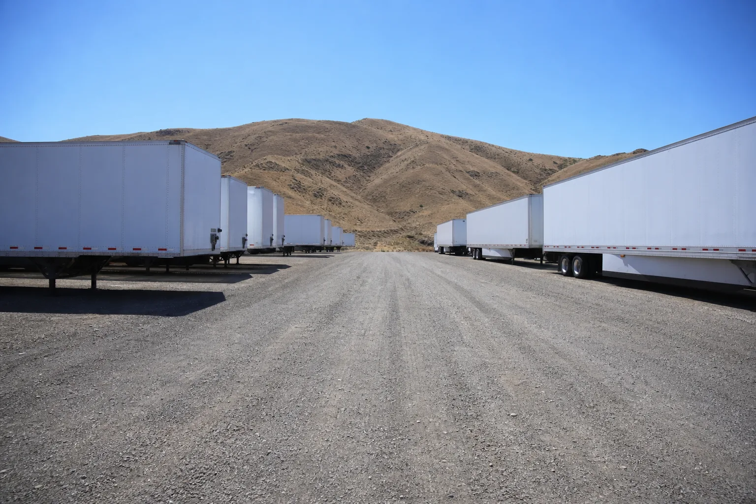 Wide gravel access lane between rows of stored semi-trailers inside the facility