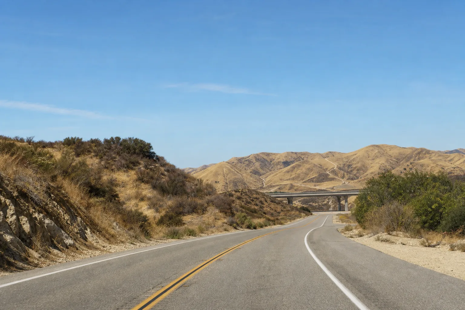 Sierra Highway curving through the Santa Clarita hills with a freeway overpass in the distance